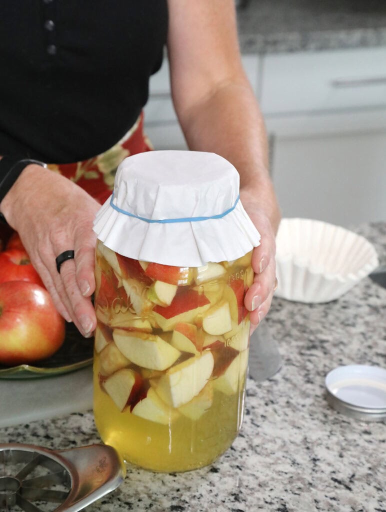 Neubert covers a jar containing apples and a honey-water mixture with a coffee filter to ferment in the process of making apple cider vinegar