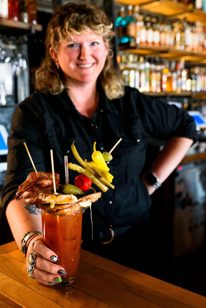Chapel Tavern bartender Alexis Neimann hands over one of the bar's famous bloody marys, topped with a grilled cheese sandwich, bacon, pickles, peppers, asparagus, string bean, olive, and lemon. Photo by Mike Higdon
