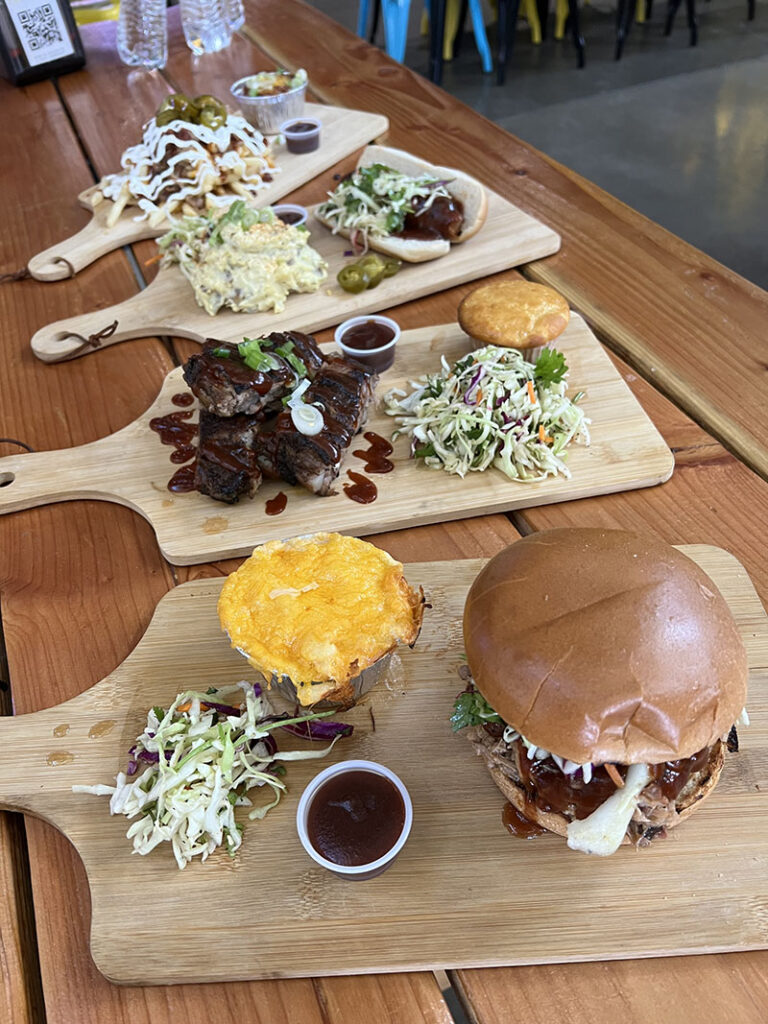 Array of barbecue dishes from Bone Appetit, including a hot link sandwich with potato salad, ribs with cornbread and cilantro-lime slaw, and pulled-pork sandwich with mac and cheese. Photo by Jessica Santina