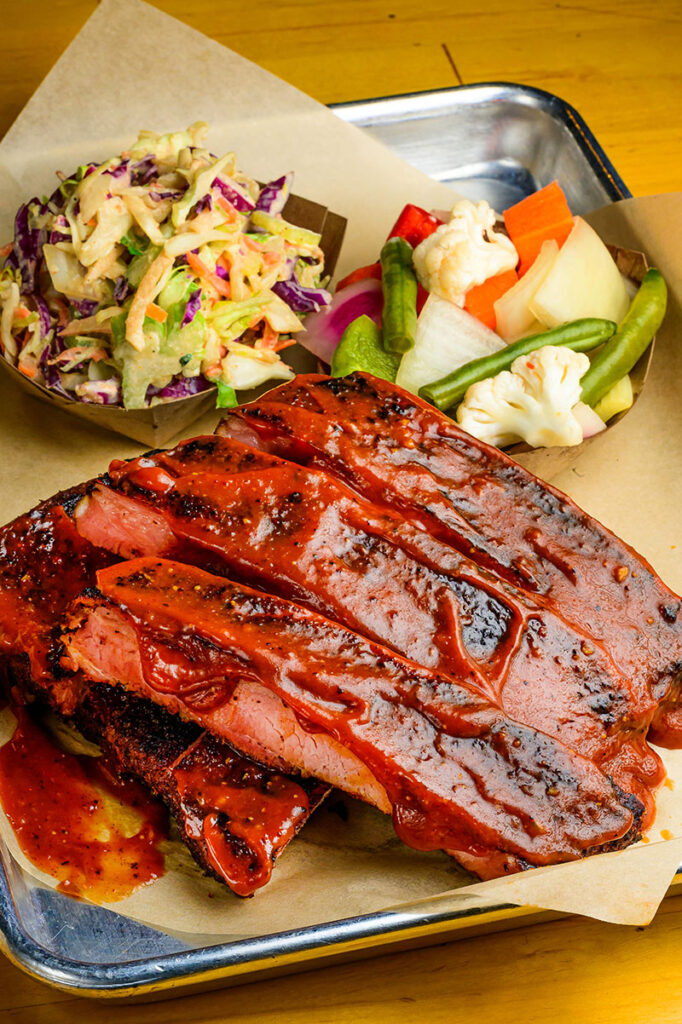 A half rack of ribs with sides of cole slaw and pickled vegetables at Butcher’s Kitchen Char-B-Que. The restaurant smokes, braises, and chars its St. Louis-style pork ribs before serving