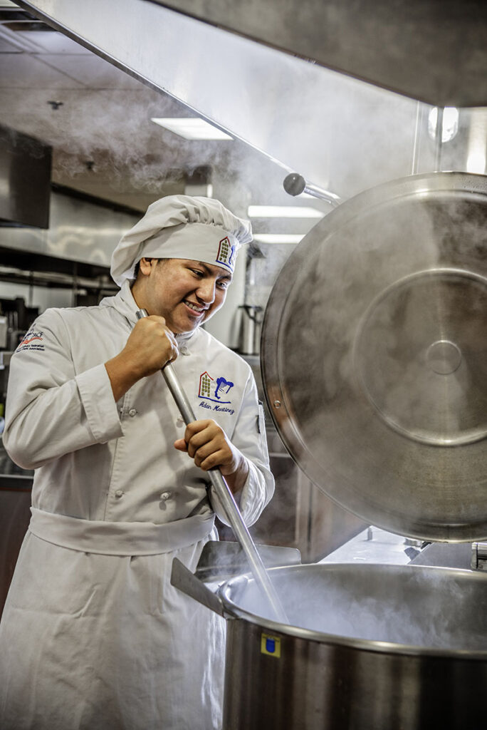 Adan Martinez stirs a steam kettle in the AACT commercial kitchen. Photo by Donna Victor