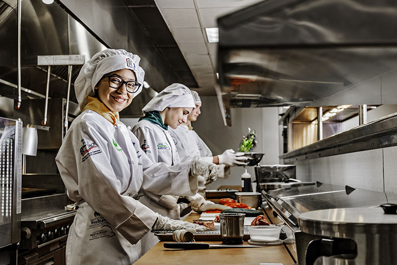 Front to back, Abigail Rodriguez, Tristin Durio, and Dillon Highline prepare ingredients in the Academy of Arts, Careers and Technology culinary program commercial kitchen. Photo by Donna Victor