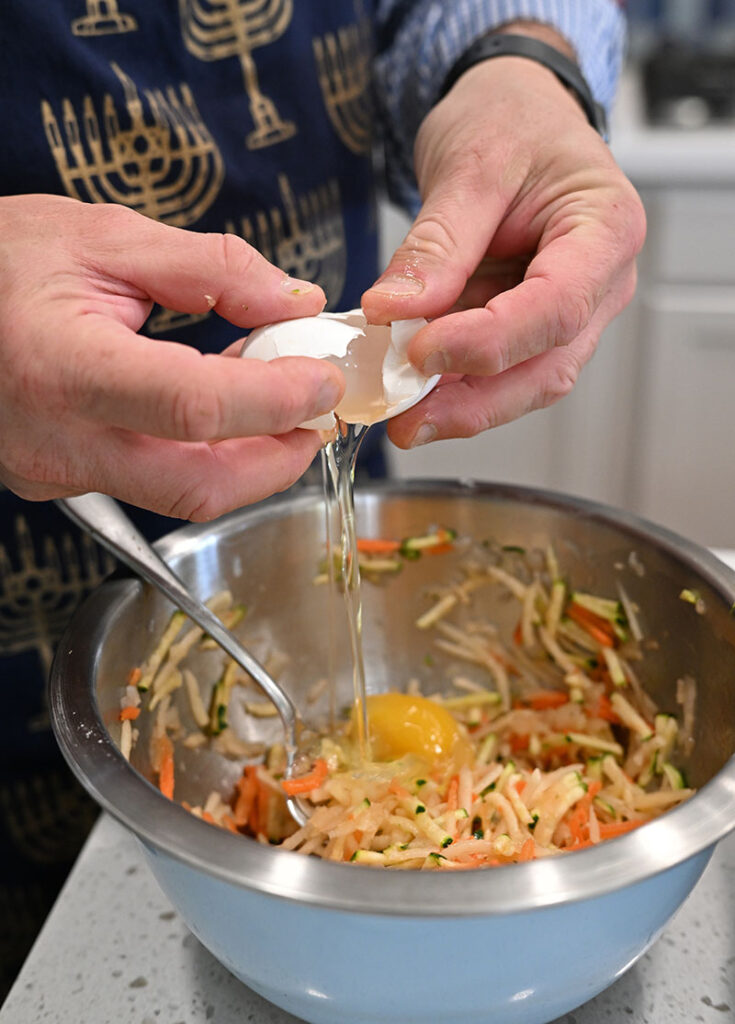 David Langer prepares the latkes with grated potatoes, onions, zucchini, carrots, and egg