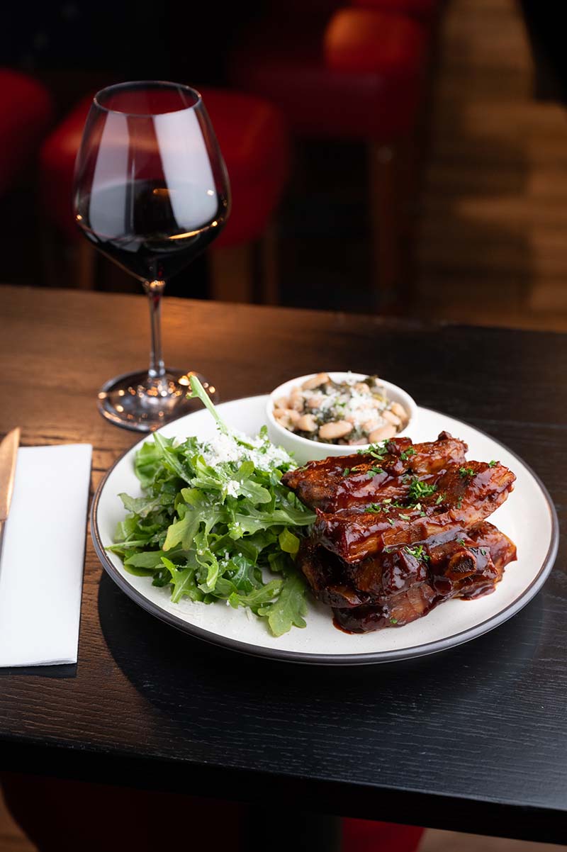 Braised short ribs in a veal demi-glaze, served with an arugula side salad and beans and greens, made with garlic, bacon, chicken stock, and Parmesan. An Italian-inspired, sommelier-curated wine list ensures a perfect wine pairing