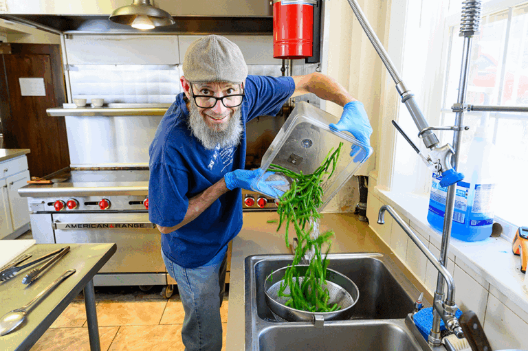Chef Kevin Ashton records his internet cooking show using his phone placed atop stacked plastic bins, inside the kitchen of the Pi Beta Phi sorority house at the University of Nevada, Reno, where he works as a private chef